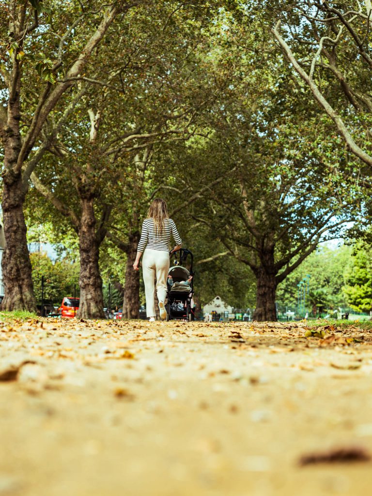 Woman walking through a park pushing her pram