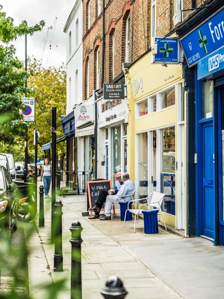 Two older gentlemen sitting have a coffee outside a cafe on a West London street