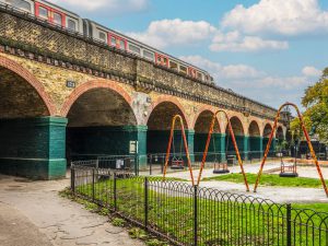 A childrens play area next to a bridge as a westbound tube flies past