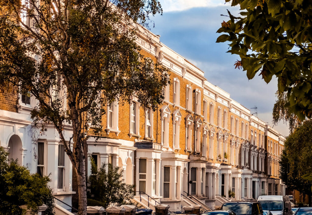 Cars parked outside orange brick houses on a tree-lined W12 street in autumn