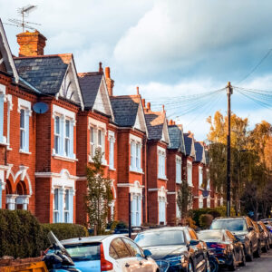 Cars parked outside red brick houses on a tree-lined W12 street in autumn