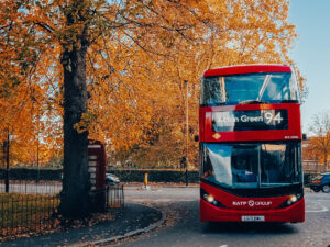 The 94 bus to Acton Green turning a corner around an autumn tree and red London phone box