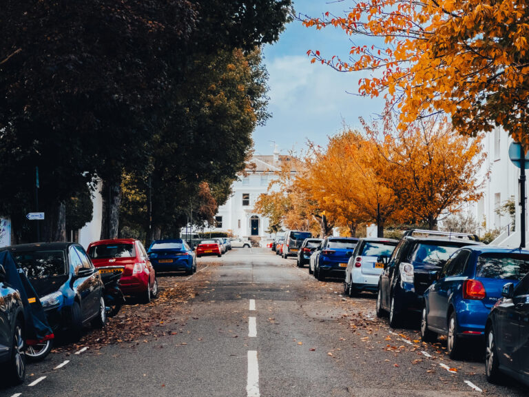Cars parked outside orange brick houses on a tree-lined W6 street in autumn